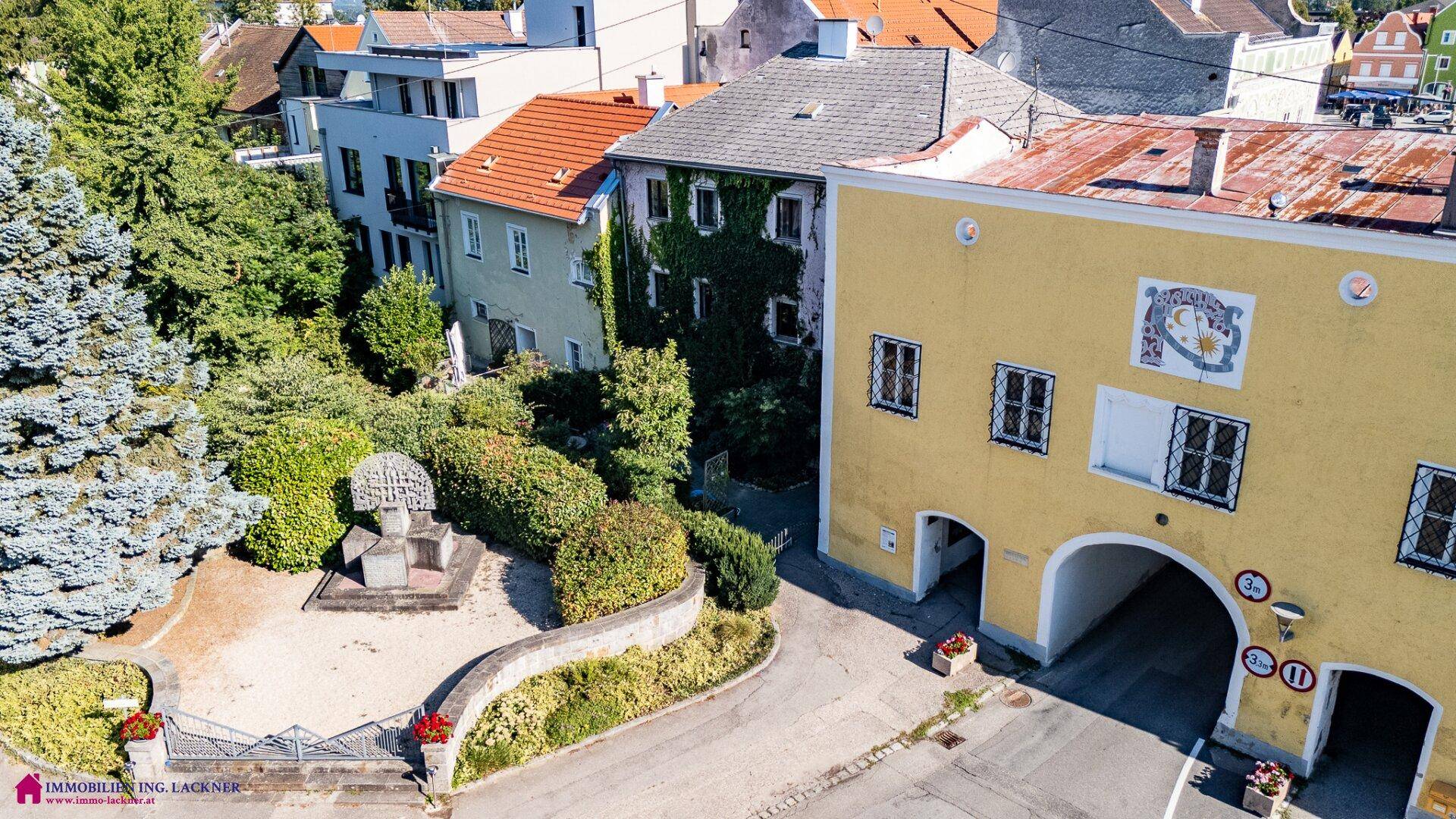 Luftaufnahme einer historischen Stadtansicht mit grünen Bäumen und traditionellen Dächern.