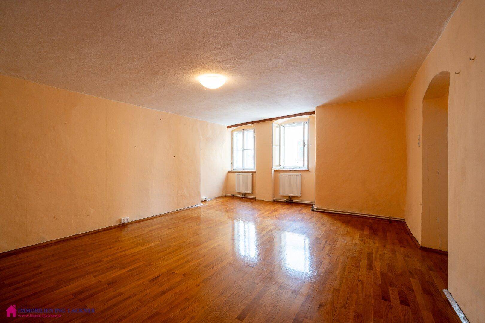 Geräumiges Wohnzimmer mit Holzboden, beigen Wänden und viel Tageslicht.