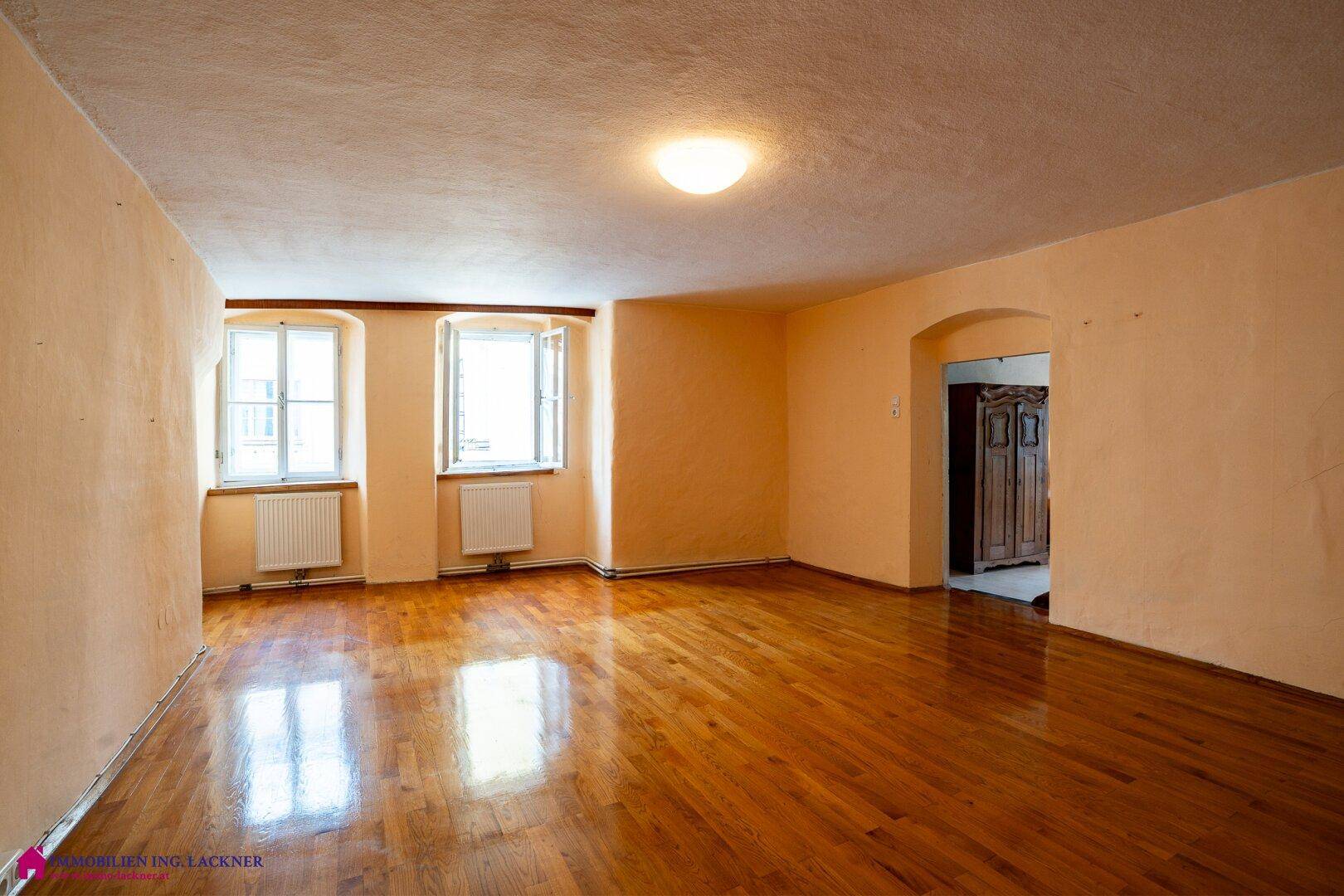 Helles Wohnzimmer mit Holzboden, beigen Wänden und zwei Fenstern.