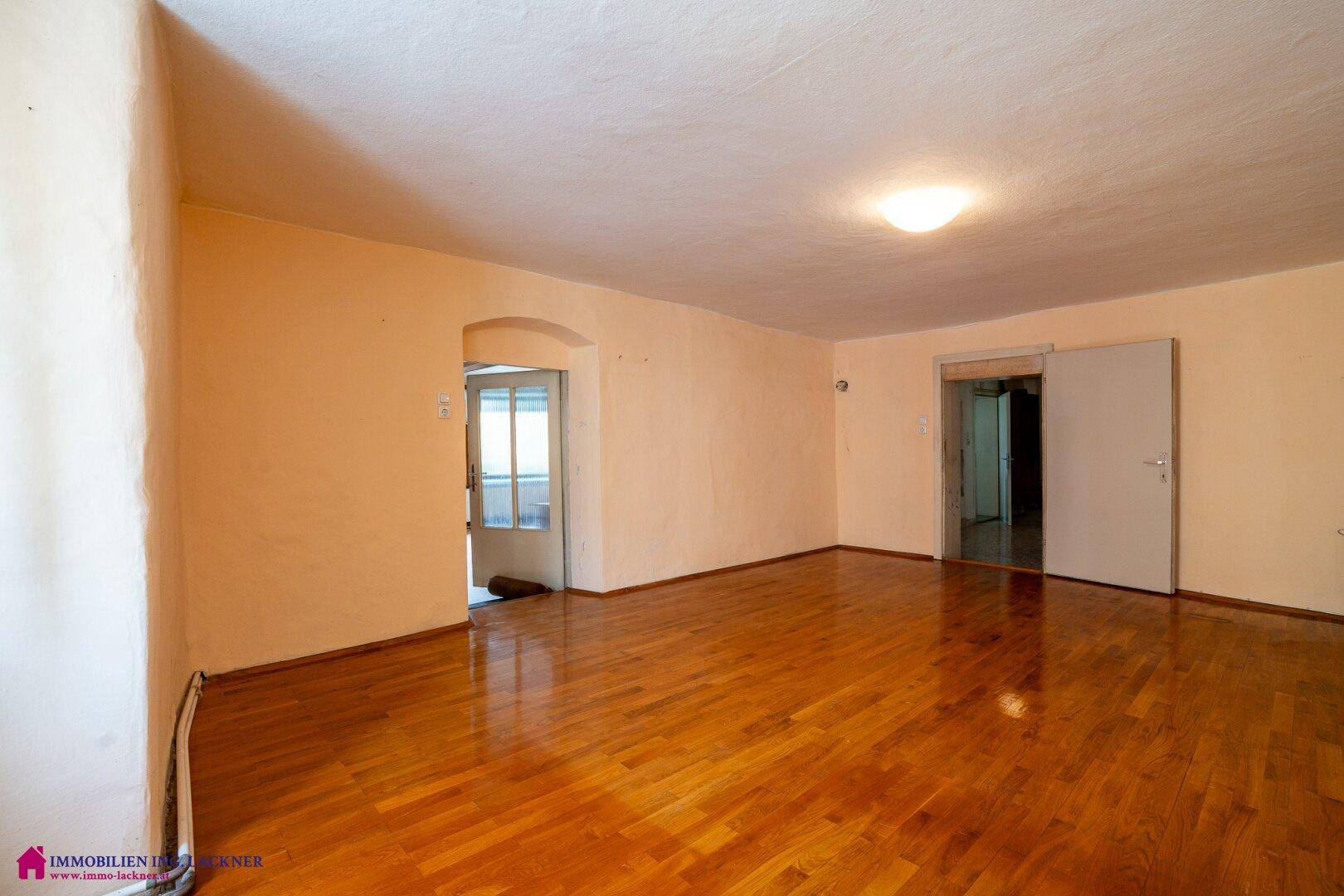 Helles Wohnzimmer mit Holzboden und Zugang zu weiteren Räumen.