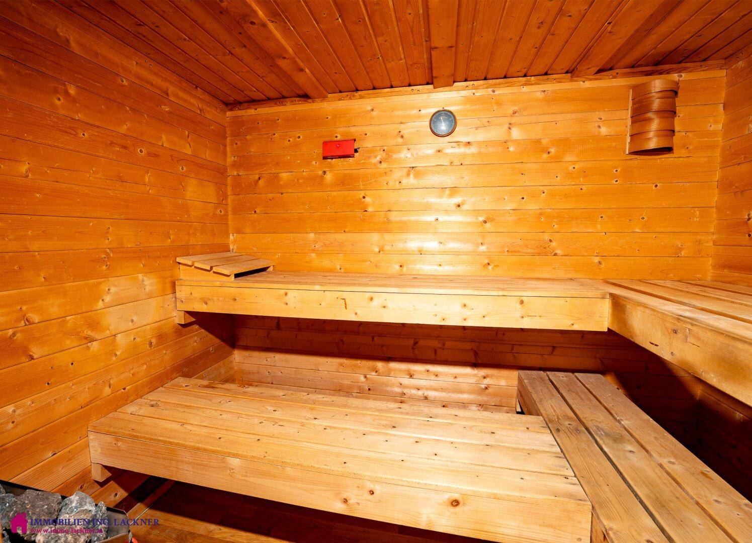 Innenansicht einer traditionellen Holzsauna mit mehreren Sitzebenen und einem Thermometer an der Wand.