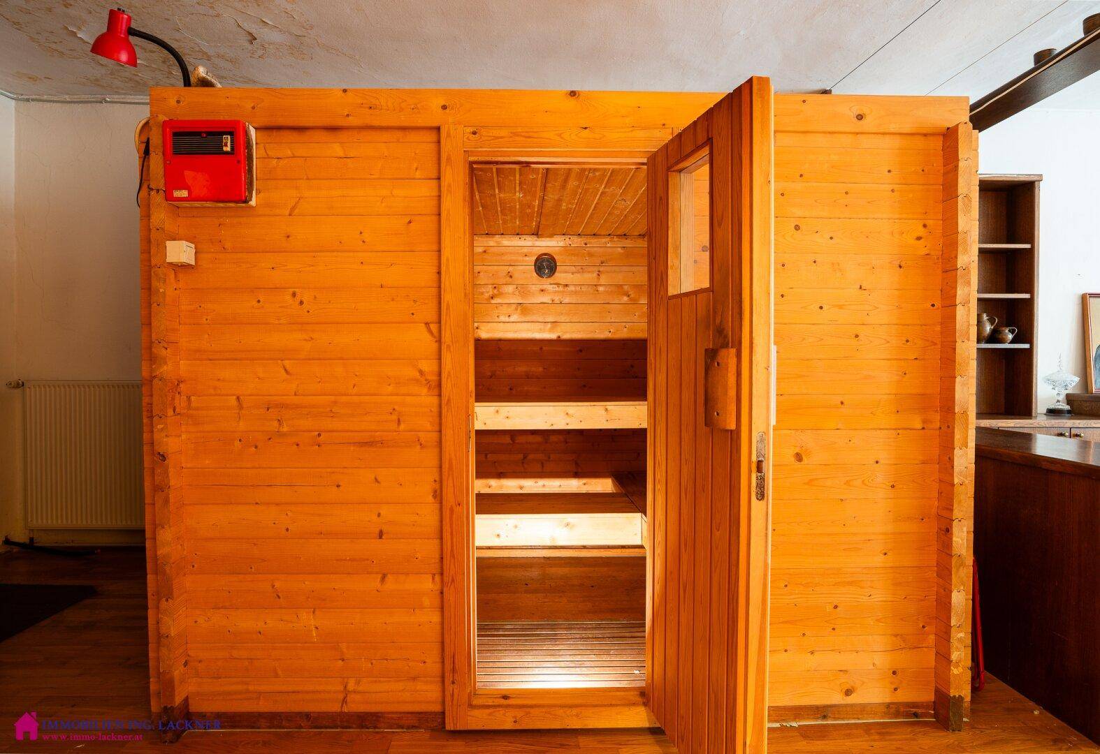 Holzkabine einer Sauna mit offener Tür und Sitzbänken im Innenbereich, Teil eines Wellnessbereichs.