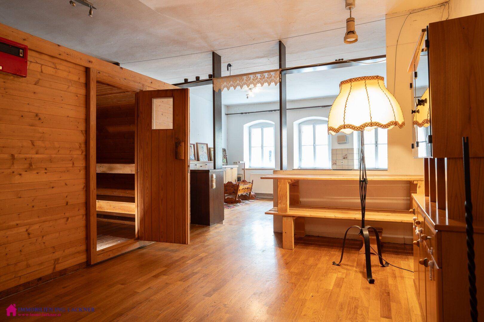 Vielseitiger Raum mit Sauna, Holzboden und einem großen Tisch.