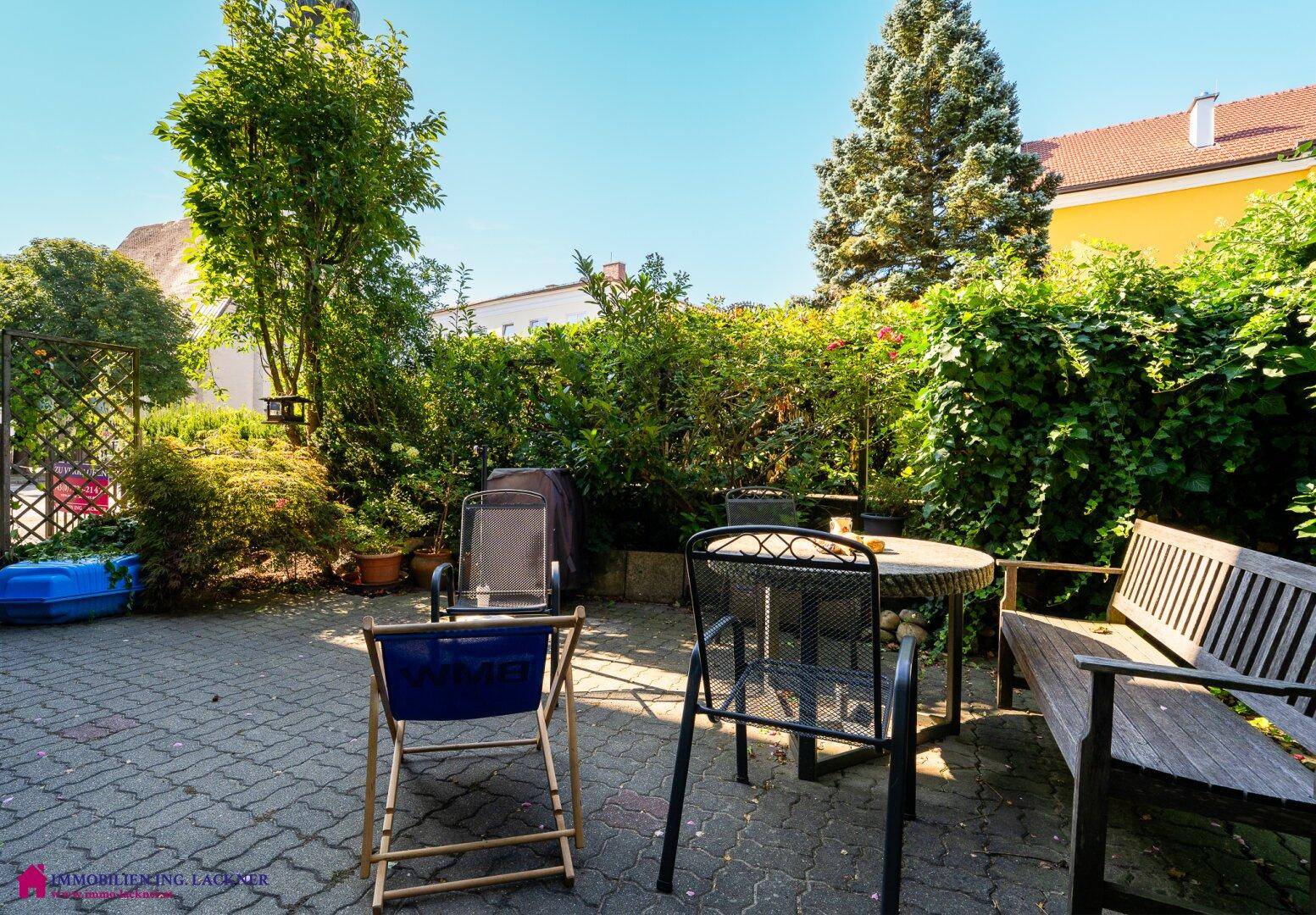 Detailansicht des gepflasterten Terrassenbereichs mit verschiedenen Gartenmöbeln und üppiger Bepflanzung.
