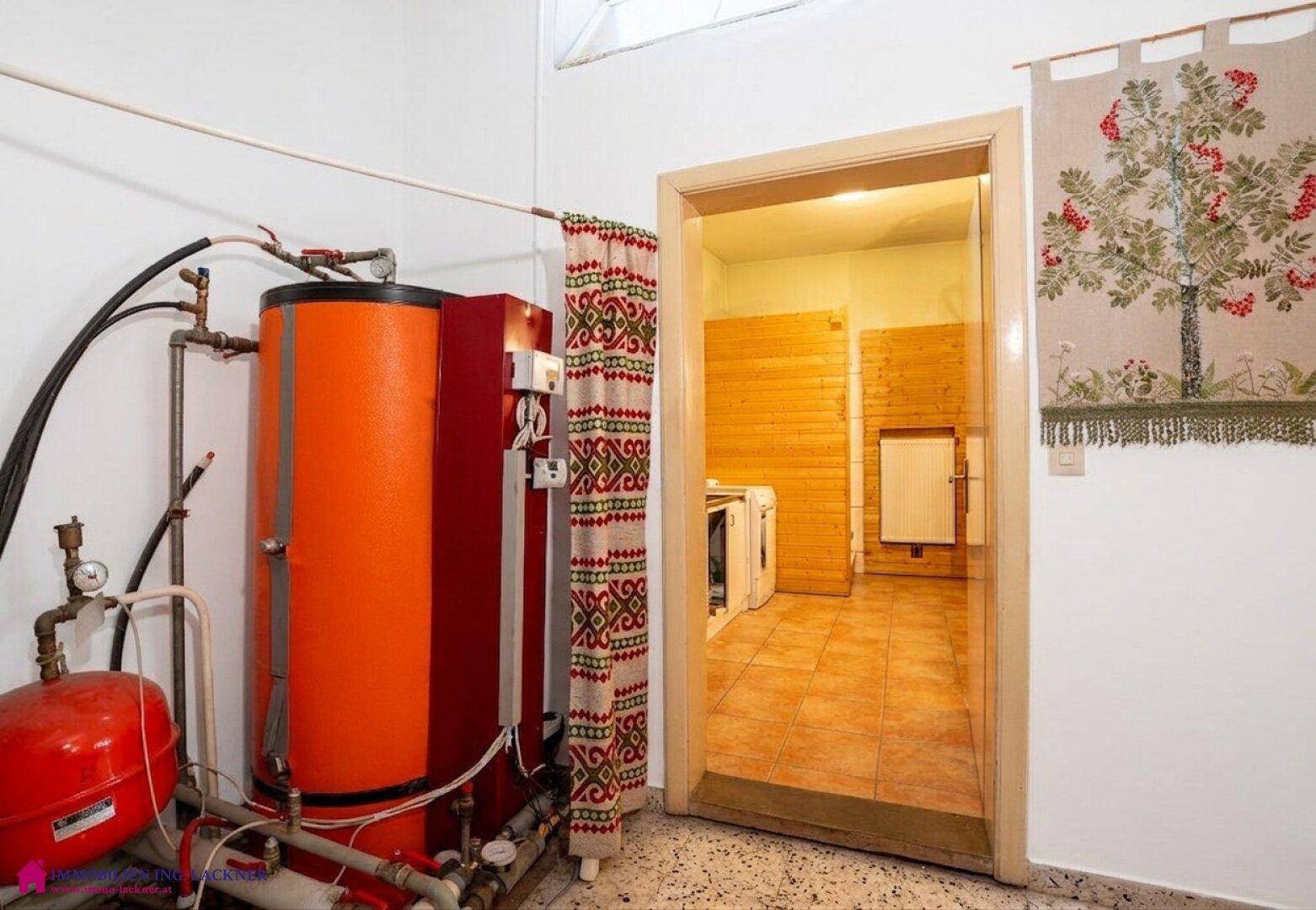 Hauswirtschaftsraum mit Warmwasserspeicher, Rohrleitungen und Blick in einen angrenzenden Raum.