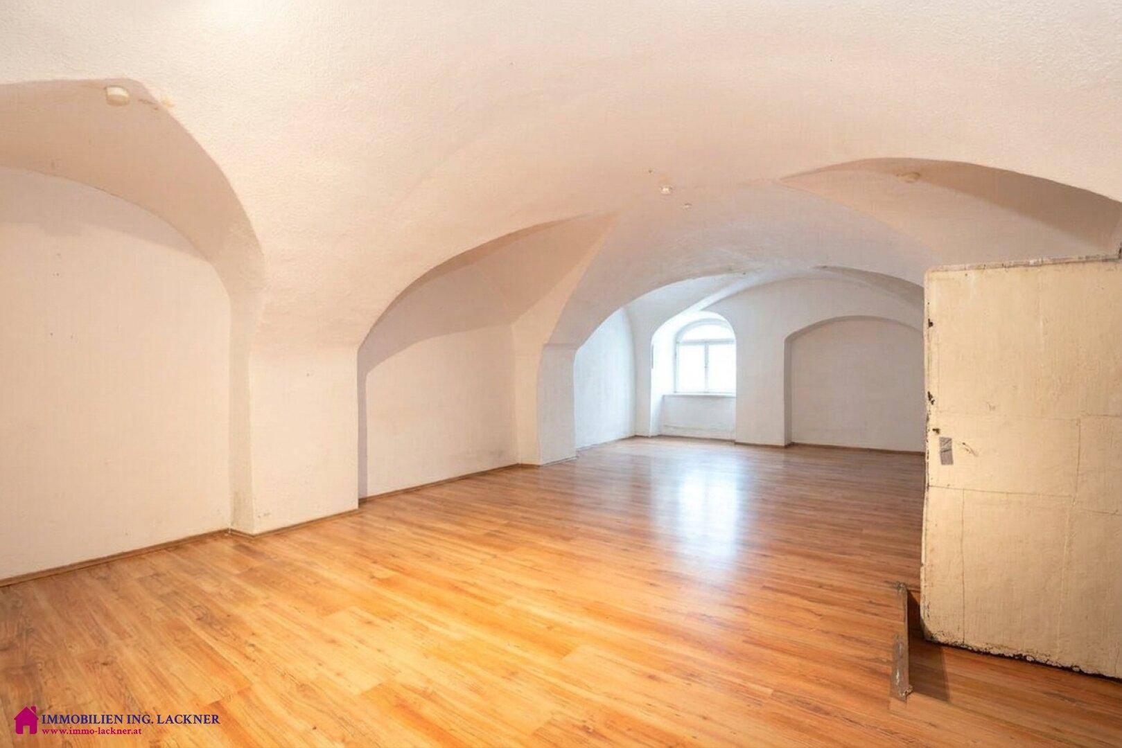 Geräumiges Wohnzimmer mit gewölbter Decke, Holzboden und einem Fenster mit viel Tageslicht.