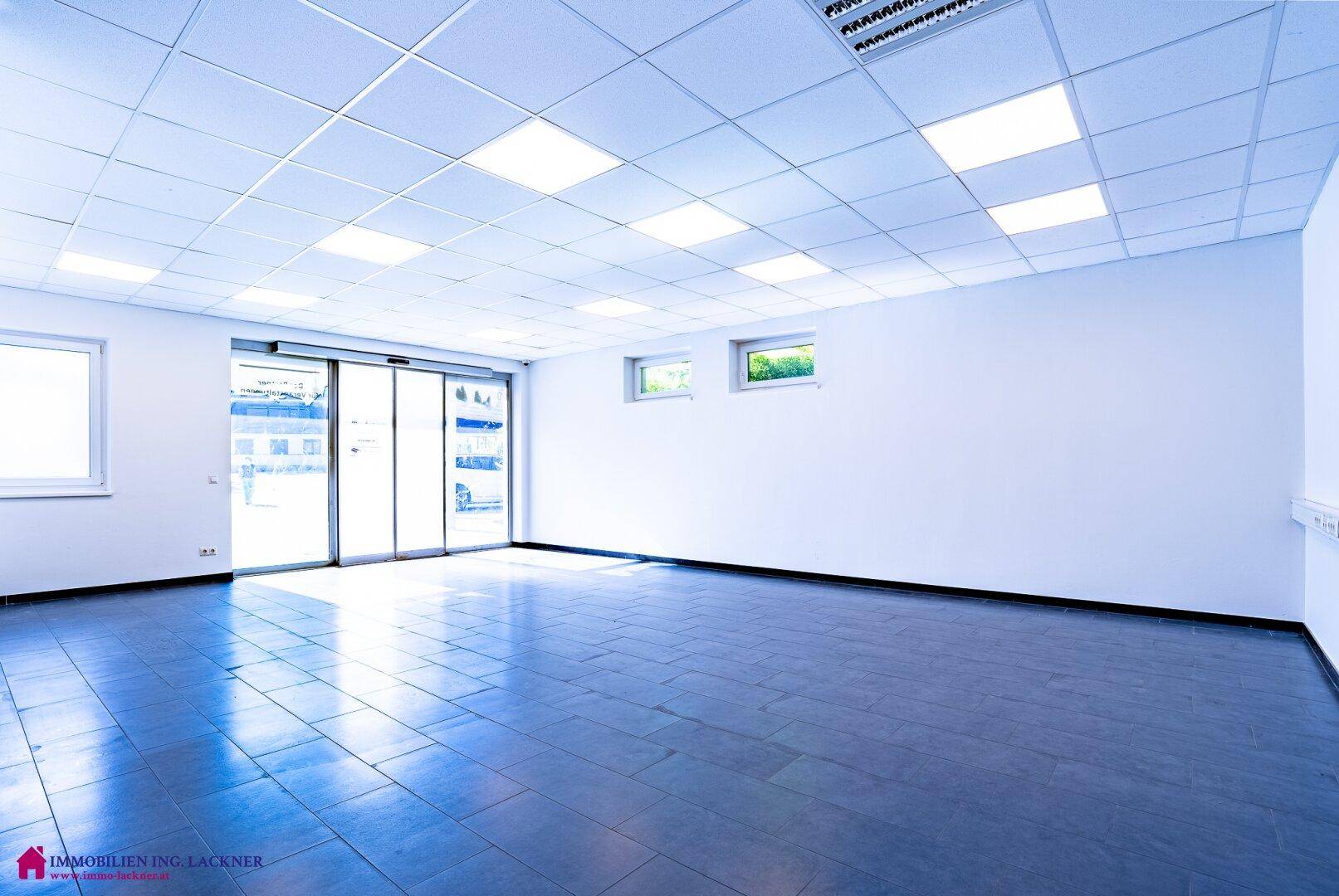 Großer, heller Büroraum mit Schiebetüren zum Außenbereich und dunklem Fliesenboden.