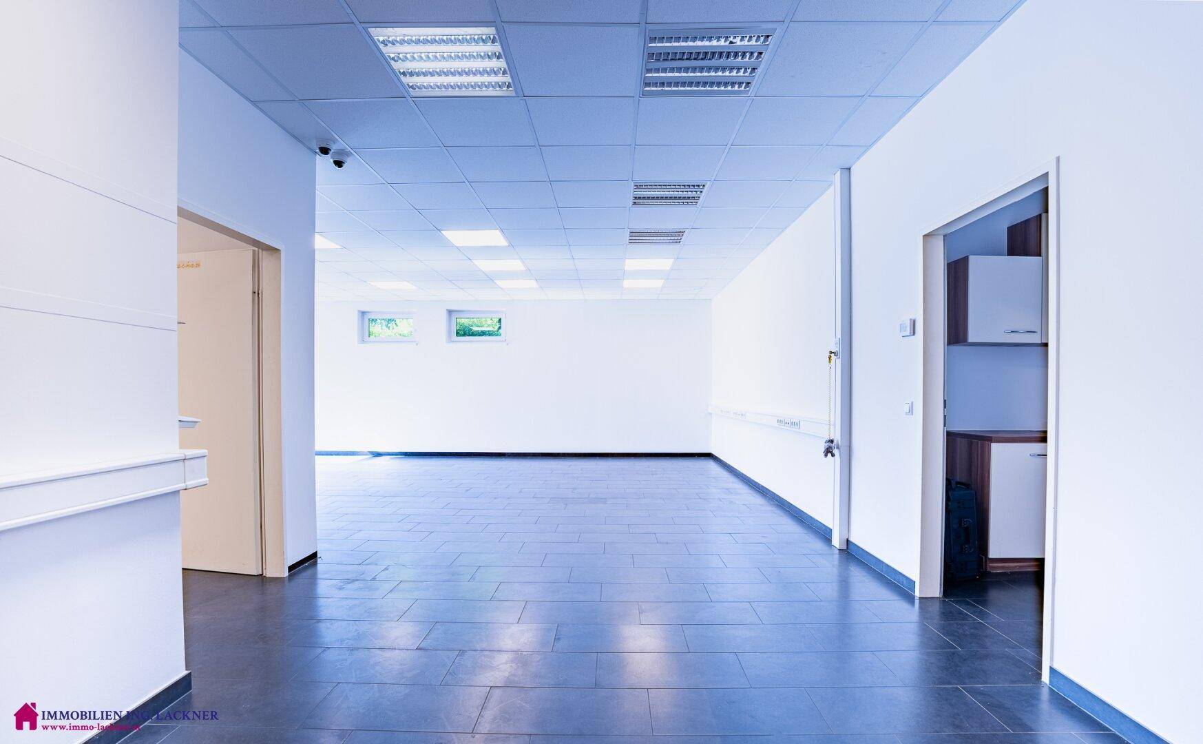 Langer, heller Flur mit dunklem Fliesenboden, weißen Wänden und Zugang zu weiteren Räumen.