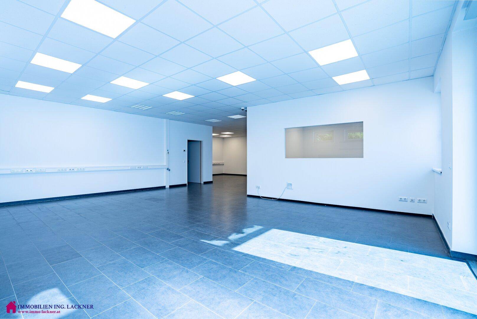 Geräumiger Büroraum mit dunklem Fliesenboden, weißen Wänden und Deckenbeleuchtung.