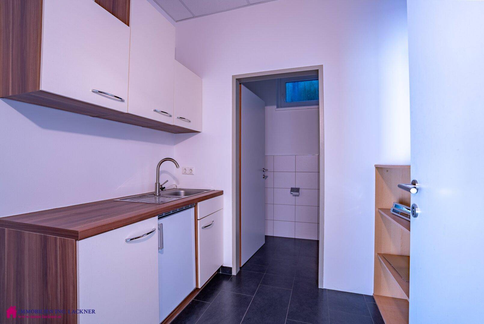 Kleine Küchenzeile mit Spüle, Unterschränken und Zugang zu einer separaten Toilette.