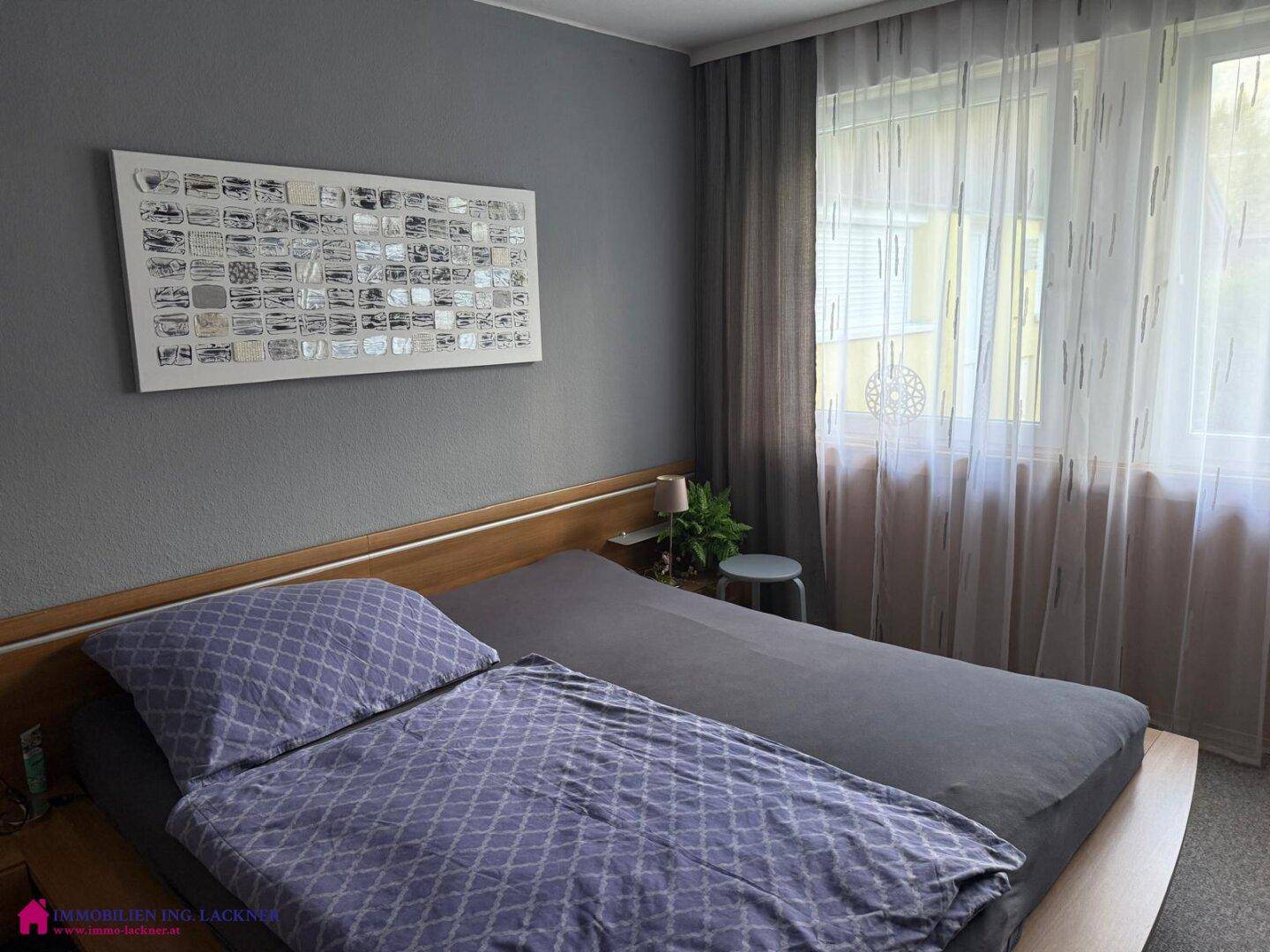 Schlafzimmer mit Doppelbett, grauen Wänden und Vorhängen, sowie natürlichem Lichteinfall.