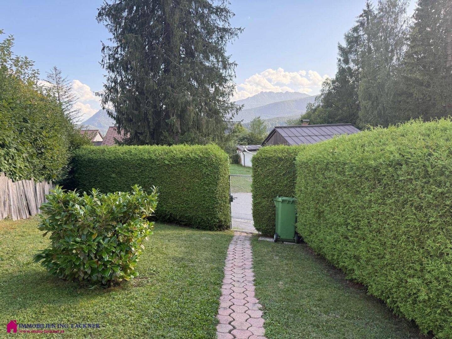 Gepflegter Garten mit Hecken, Rasenfläche und einem Weg, der zum Tor führt.