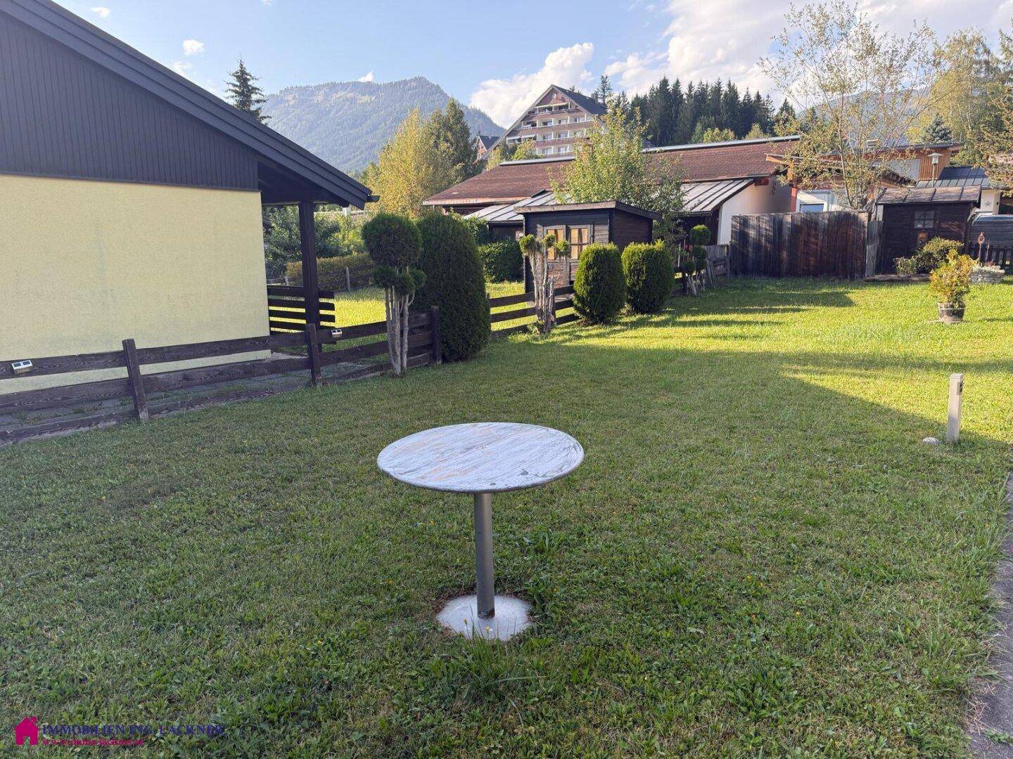 Weitläufige Rasenfläche im Garten mit einem kleinen Tisch und Bergblick.