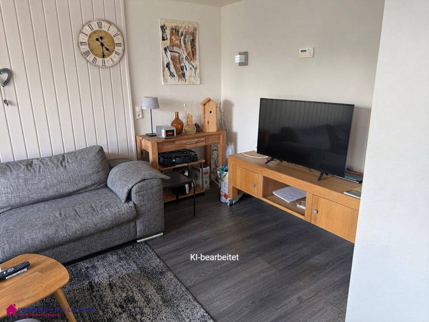 Helles Wohnzimmer mit modernem Laminatboden, bequemer Couch und Fernseher.
