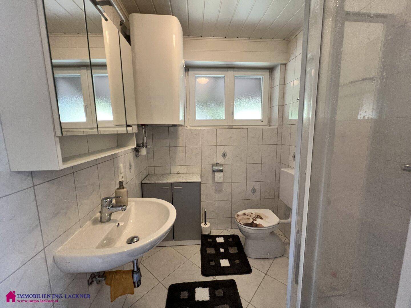 Helles Badezimmer mit Dusche, Waschbecken, WC und Fenster für natürliche Belüftung.