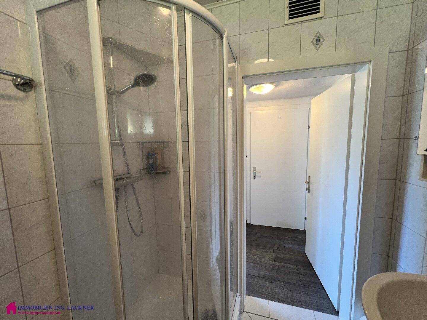 Duschkabine im gefliesten Badezimmer mit Blick auf den Flur, funktional und sauber.