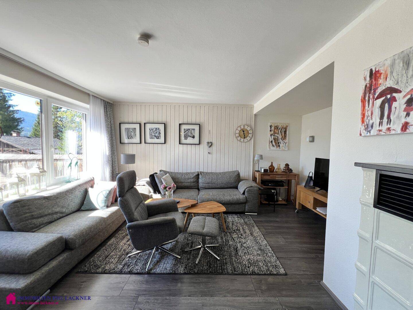 Gemütliches Wohnzimmer mit Kachelofen, bequemer Couch und Blick ins Grüne.