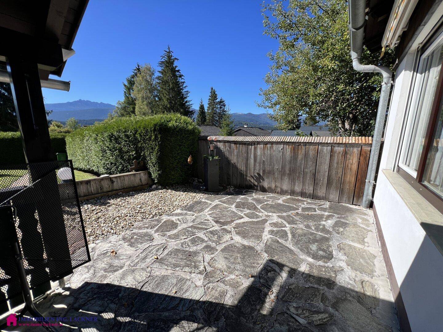 Sonniger Terrassenbereich mit Steinplatten und weitem Blick auf die umliegende Berglandschaft.