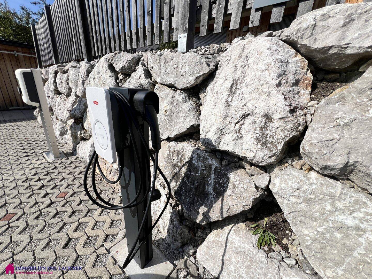 Ladestation für Elektrofahrzeuge vor einer rustikalen Steinfassade.