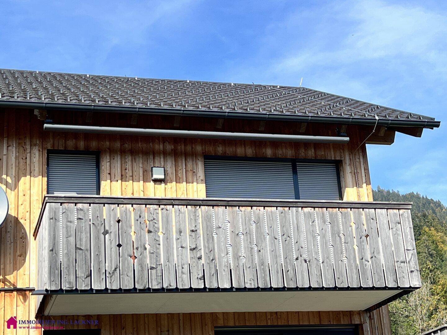 Holzfassade eines Hauses mit einem traditionellen Holzbalkon und geschlossenen Rollläden.