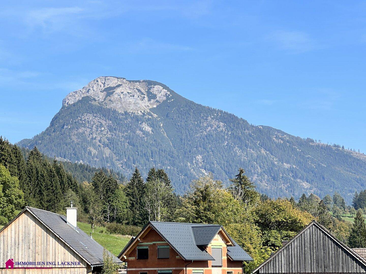Panoramablick auf majestätische Berge und umliegende Häuser unter klarem blauem Himmel.