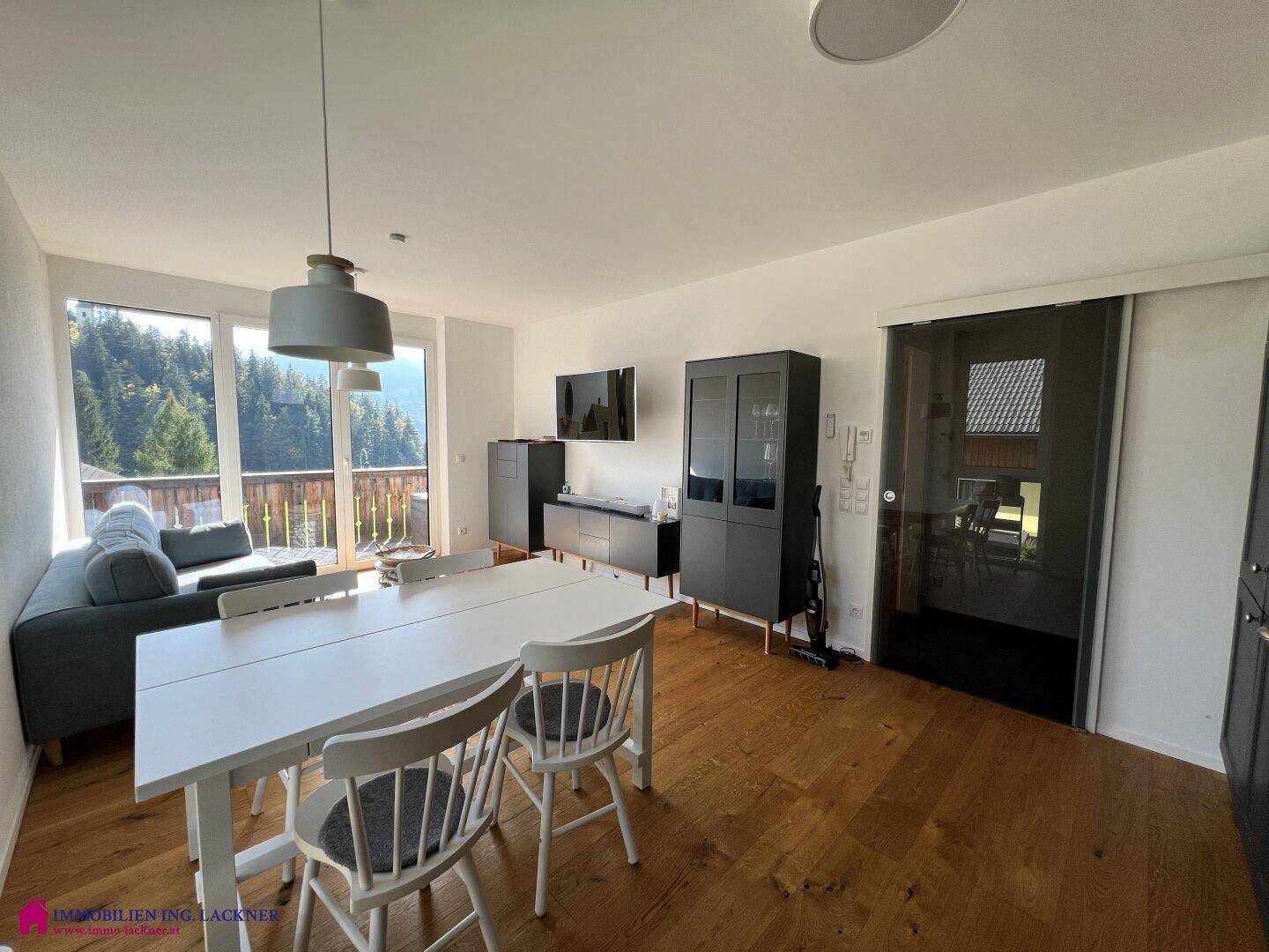 Geräumiger Wohn-Essbereich mit Holzboden, Esstisch und Zugang zu einem Balkon mit Aussicht.