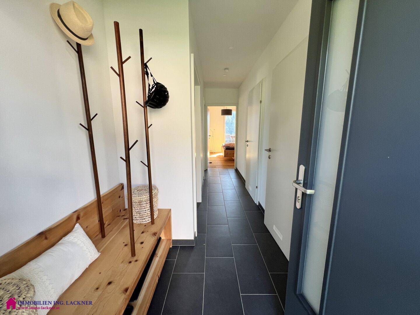Heller Flur mit dunklen Fliesen, Garderobe aus Holz und einer Sitzbank.
