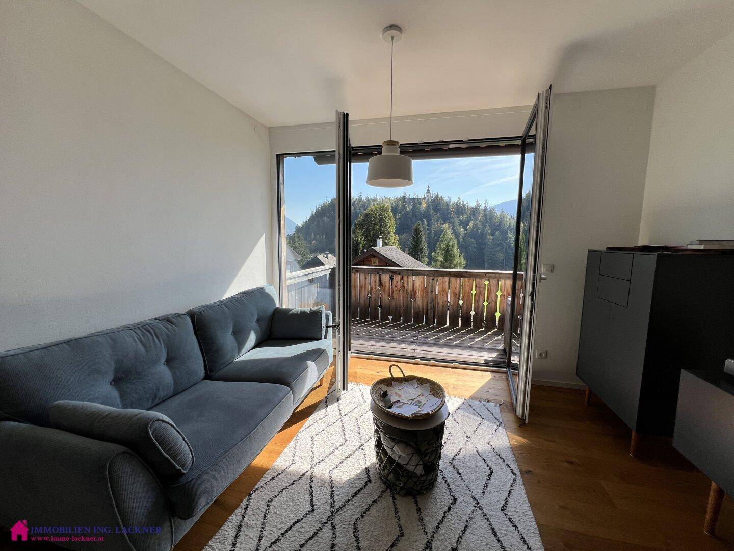 Helles Wohnzimmer mit bequemer Couch, Holzboden und direktem Zugang zum Balkon mit Bergblick.