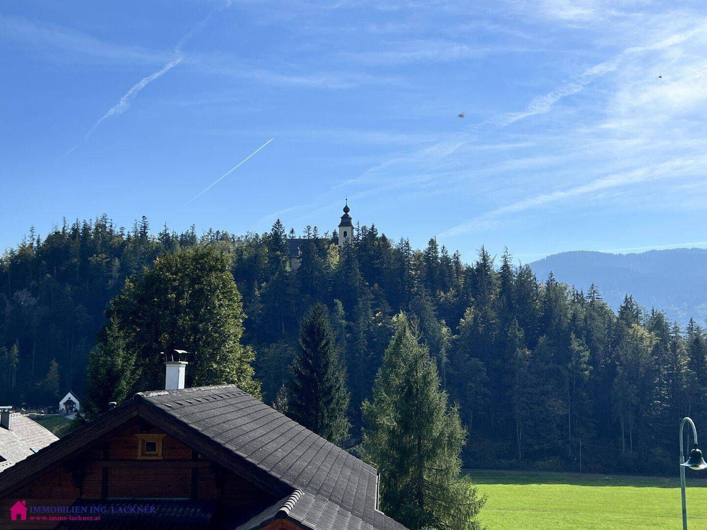 Malerischer Blick auf eine Kirche auf einem bewaldeten Hügel unter blauem Himmel.