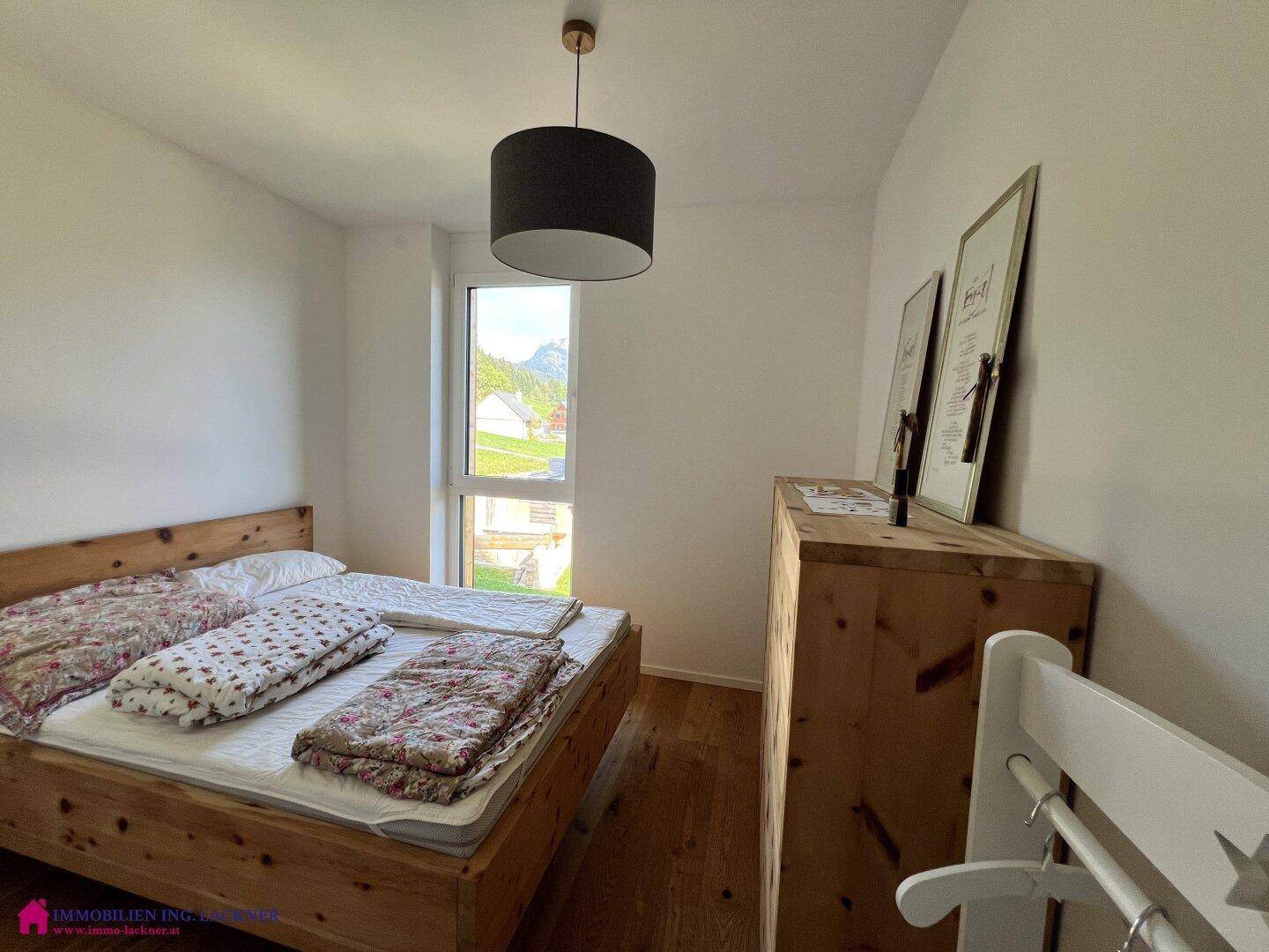 Gemütliches Schlafzimmer mit Holzbett, Holzboden und Fenster mit Blick ins Grüne.