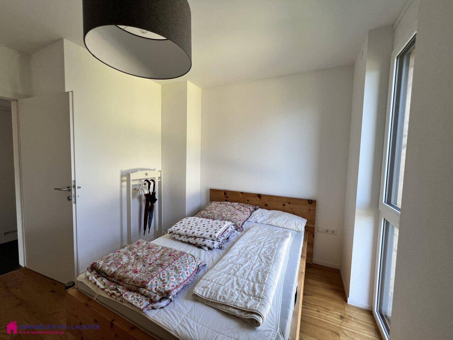 Schlafzimmer mit Holzbett, Holzboden und großem Fenster für viel Tageslicht.