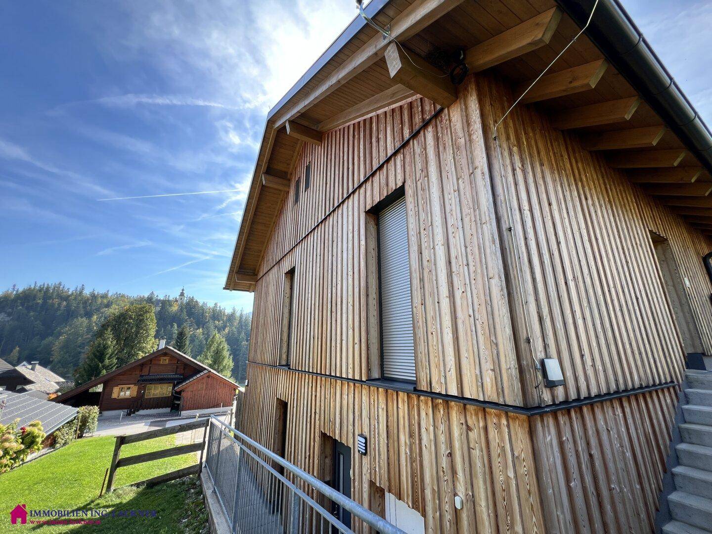Seitenansicht eines modernen Holzhauses mit vertikaler Holzverkleidung und großen Fenstern.