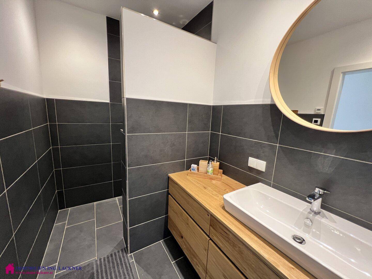 Modernes Badezimmer mit Holzwaschtisch, Spiegel und offenem Zugang zur Duschkabine.