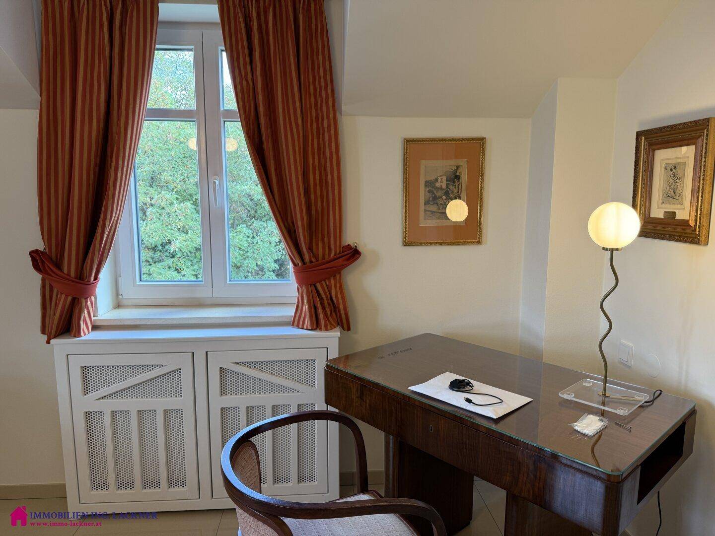 Helles Arbeitszimmer mit Holzschreibtisch, Fensterblick ins Grüne und eleganten Vorhängen.