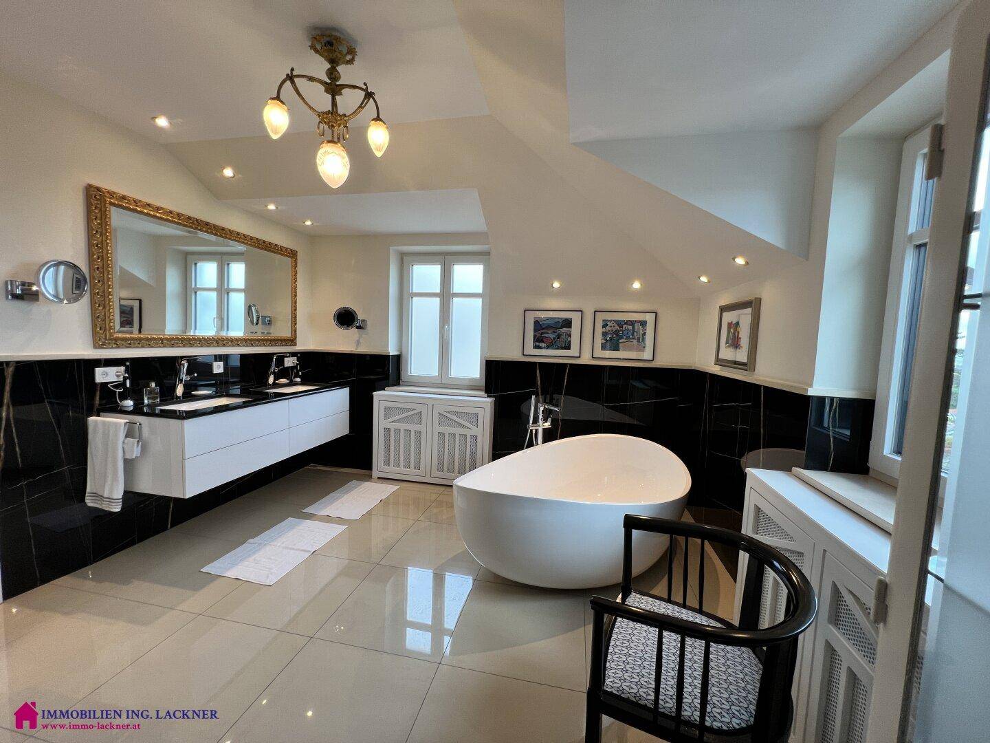 Luxuriöses Badezimmer mit freistehender Badewanne, Doppelwaschbecken und schwarzen Fliesen.