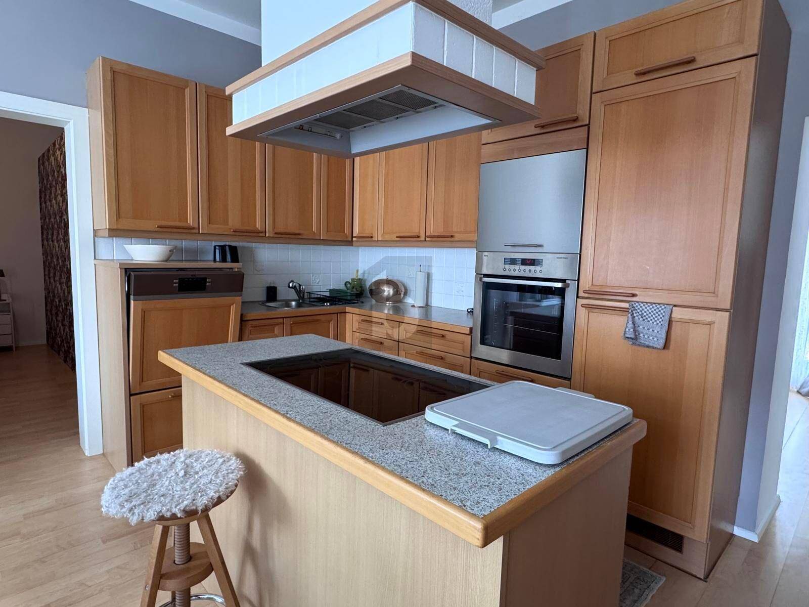 Gemütliche Küche mit Holzschränken, integrierten Geräten und einer Kücheninsel mit Kochfeld.
