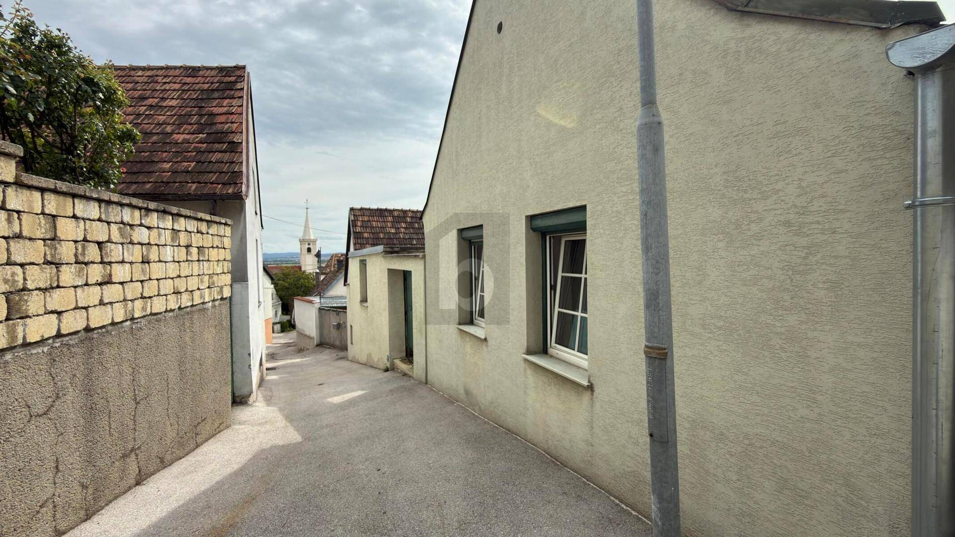 Schmale Gasse zwischen Häusern mit Blick auf einen Kirchturm in der Ferne.