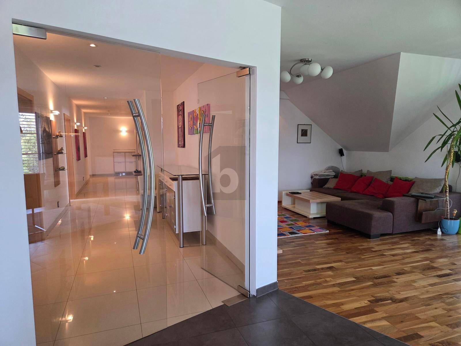 Heller Flur mit gläsernen Türen und Blick in ein gemütliches Wohnzimmer mit Holzboden.