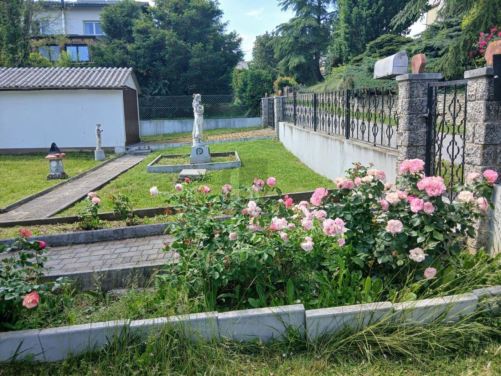 Blühender Rosengarten mit gepflastertem Weg und dekorativen Elementen im Vorgartenbereich.