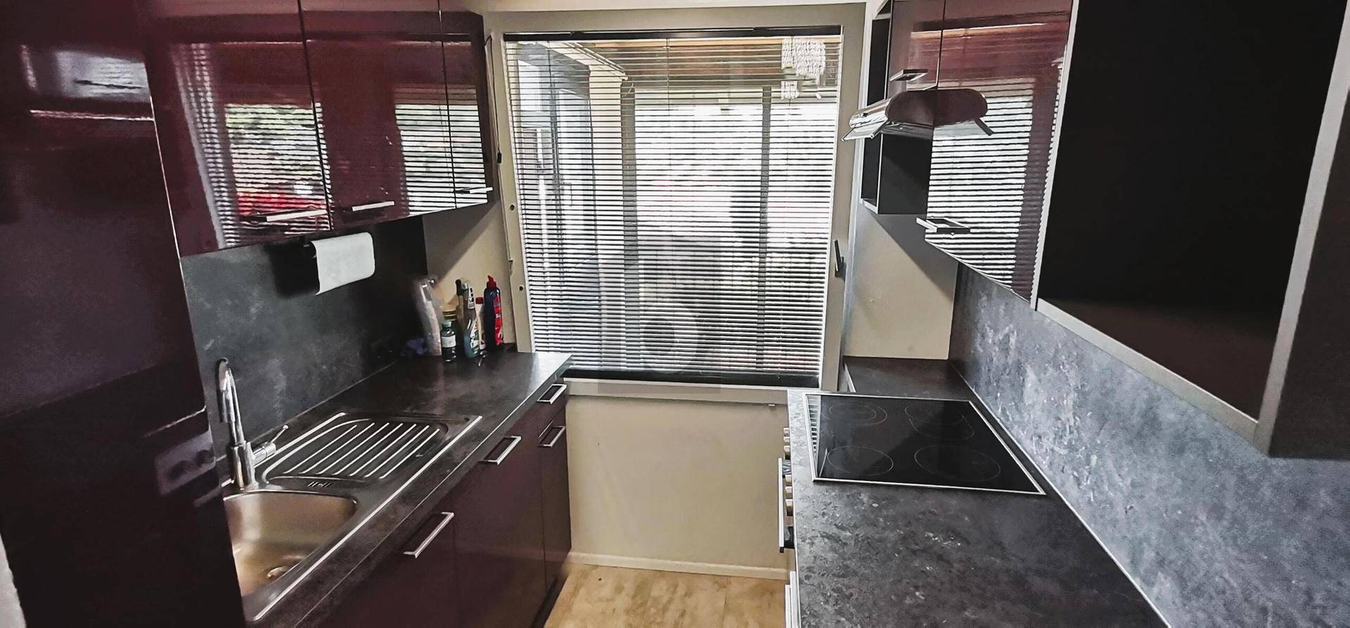 Moderne Küche mit dunklen Hochglanzschränken, Spüle und Induktionskochfeld am Fenster.