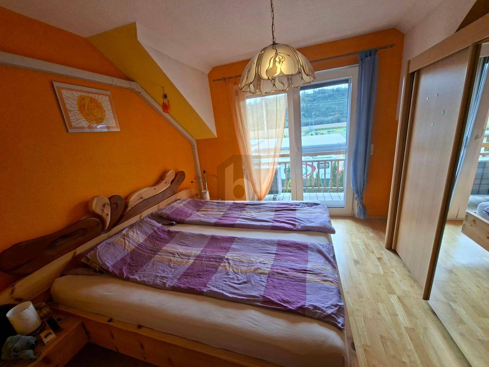 Gemütliches Schlafzimmer mit Holzbett, orangefarbenen Wänden und Balkonzugang.