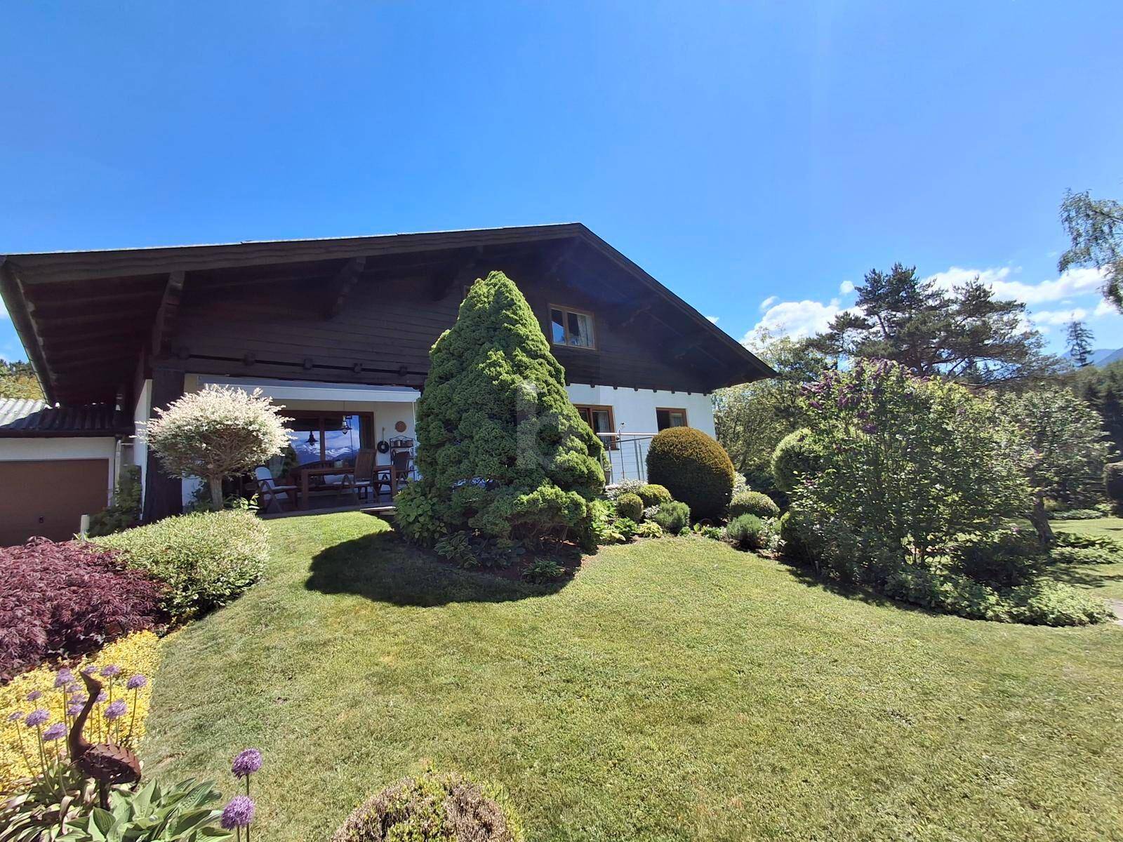 Seitlicher Blick auf das Haus mit üppigem Garten, Terrasse und weitem Blick in die Landschaft.