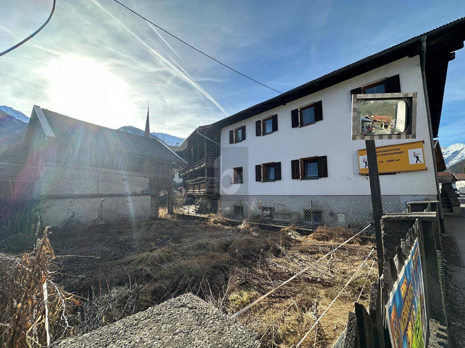 Seitenansicht eines traditionellen Gebäudes mit angrenzendem, ungenutztem Grundstück und Bergblick.