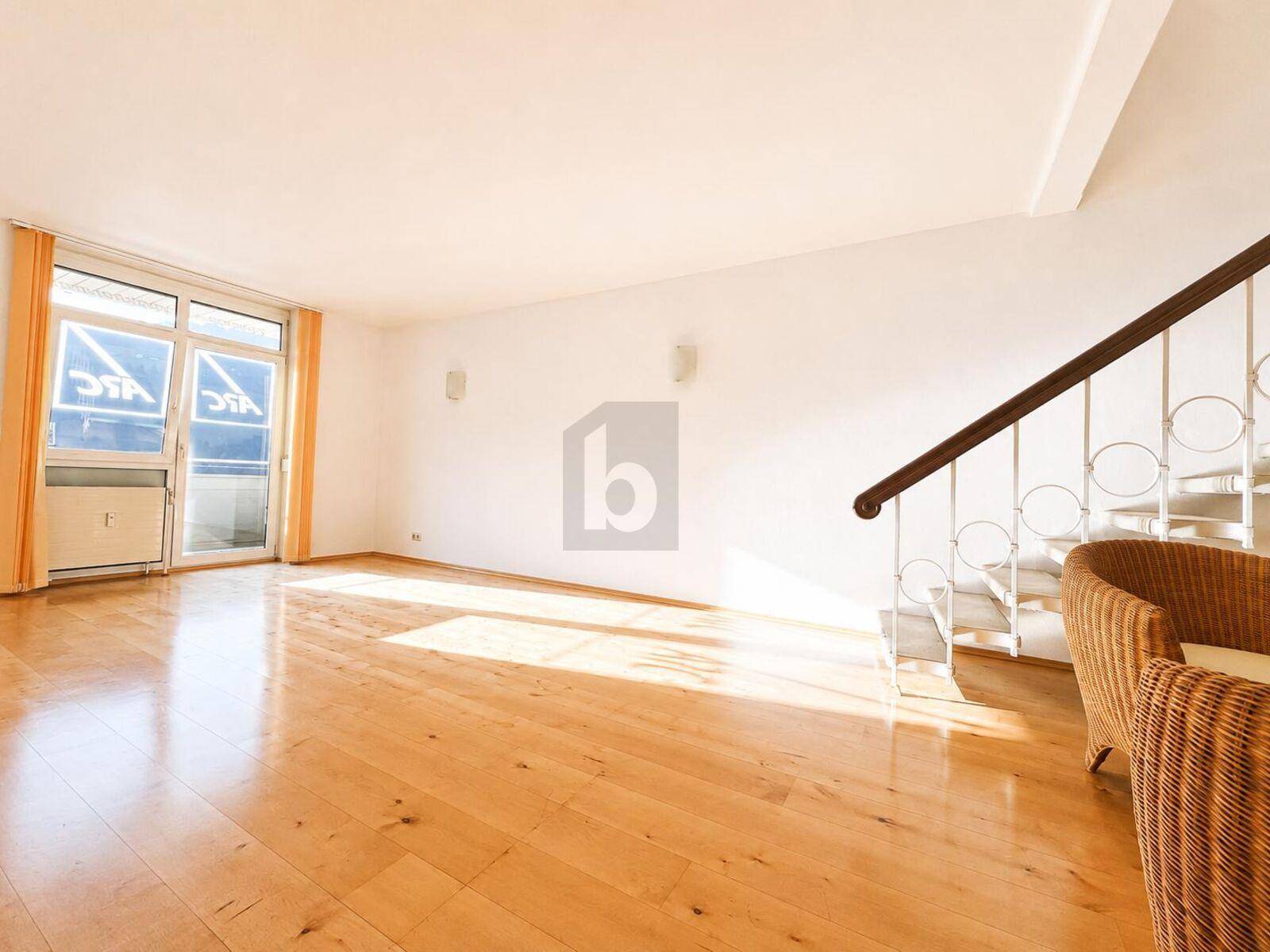 Helles Wohnzimmer mit Holzboden und Zugang zu einem kleinen Balkon, ergänzt durch eine elegante Treppe.
