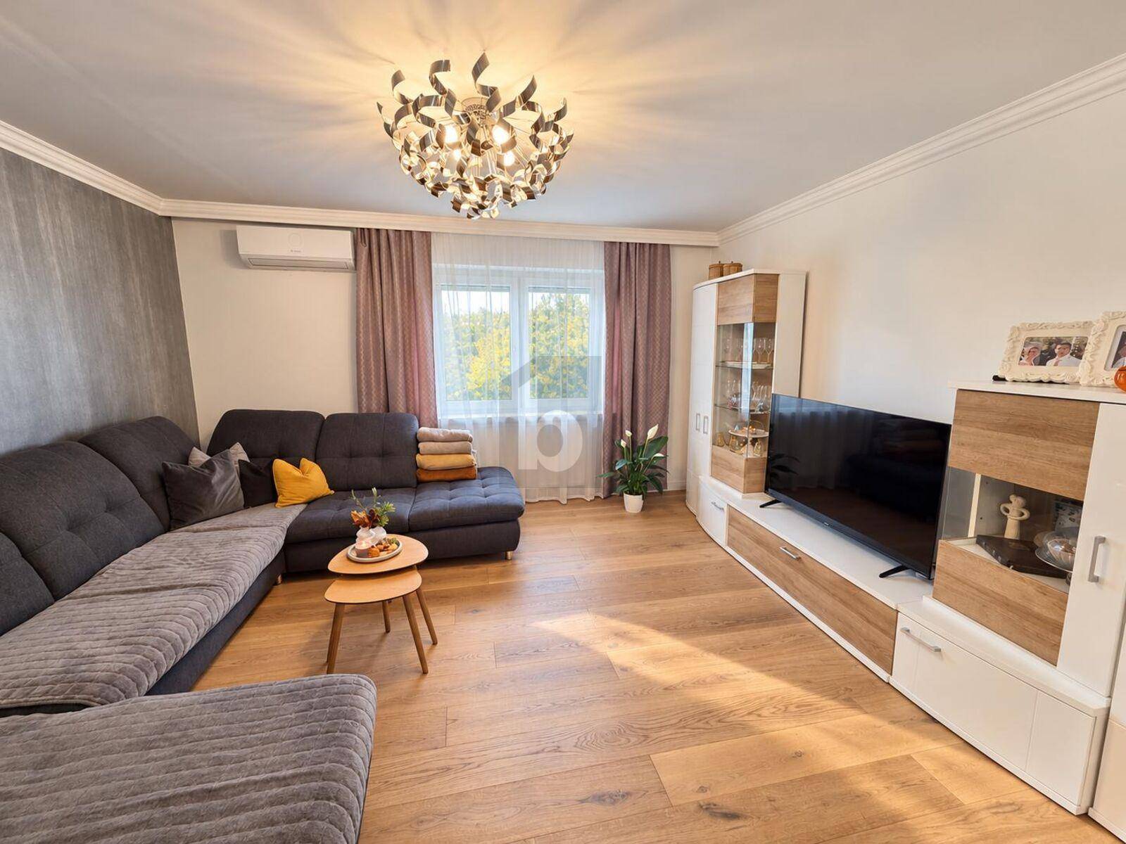Modernes Wohnzimmer mit großem Ecksofa, Holzboden und dekorativer Deckenleuchte.