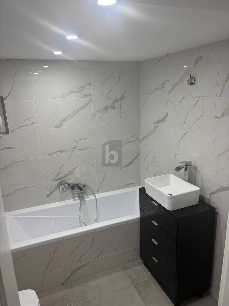 Modernes Badezimmer mit weißen Marmorfliesen, Badewanne und stilvollem Waschtisch.