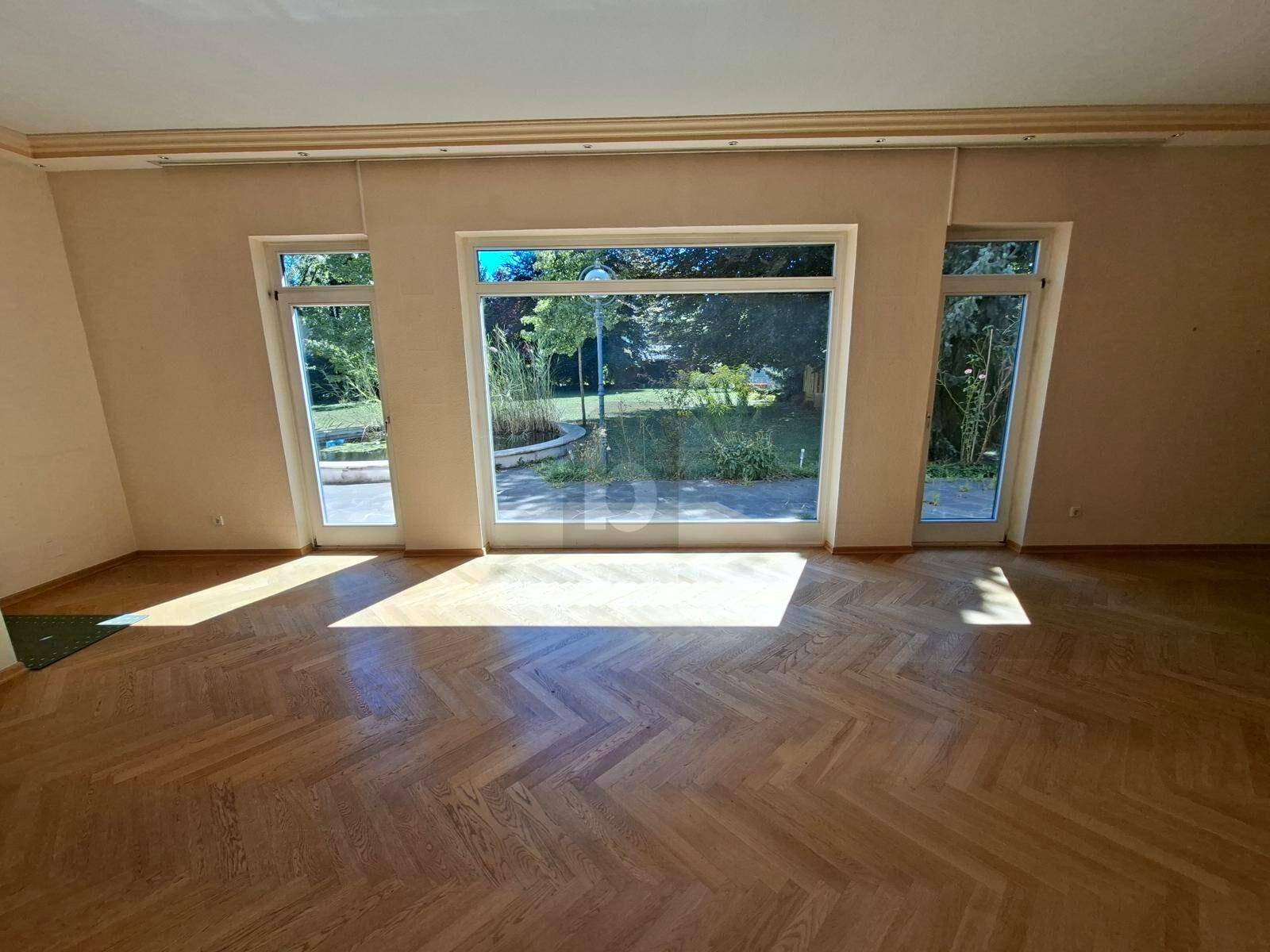 Helles Wohnzimmer mit Fischgrätparkett und großen Fenstern mit Blick auf den Garten.