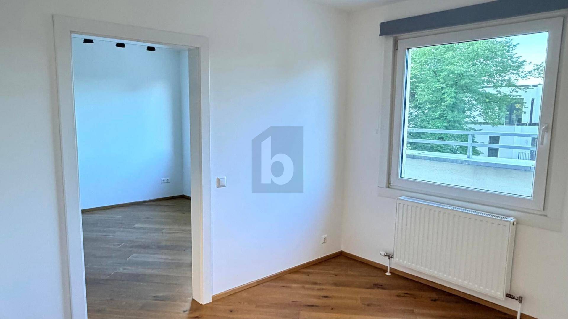 Freundliches Zimmer mit Parkettboden und Fenster, das viel Tageslicht hereinlässt.