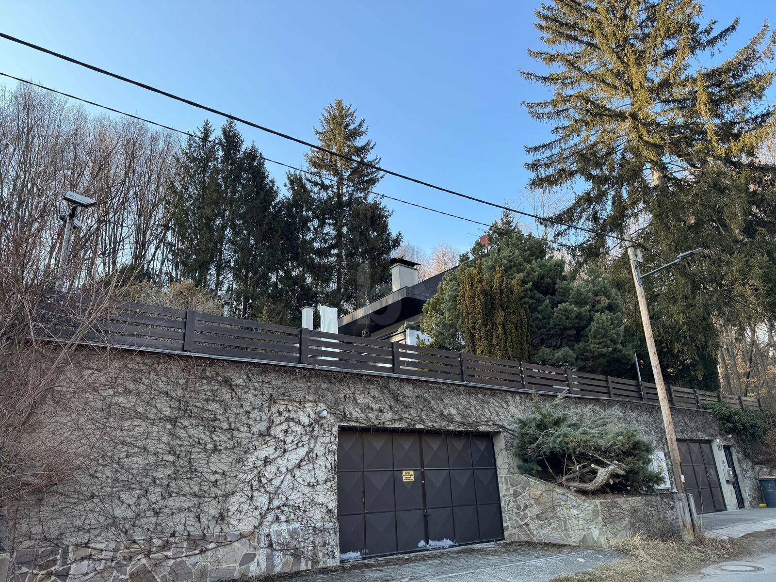 Hausfassade mit integrierter Garage und bewachsenen Steinmauern von der Straße aus.