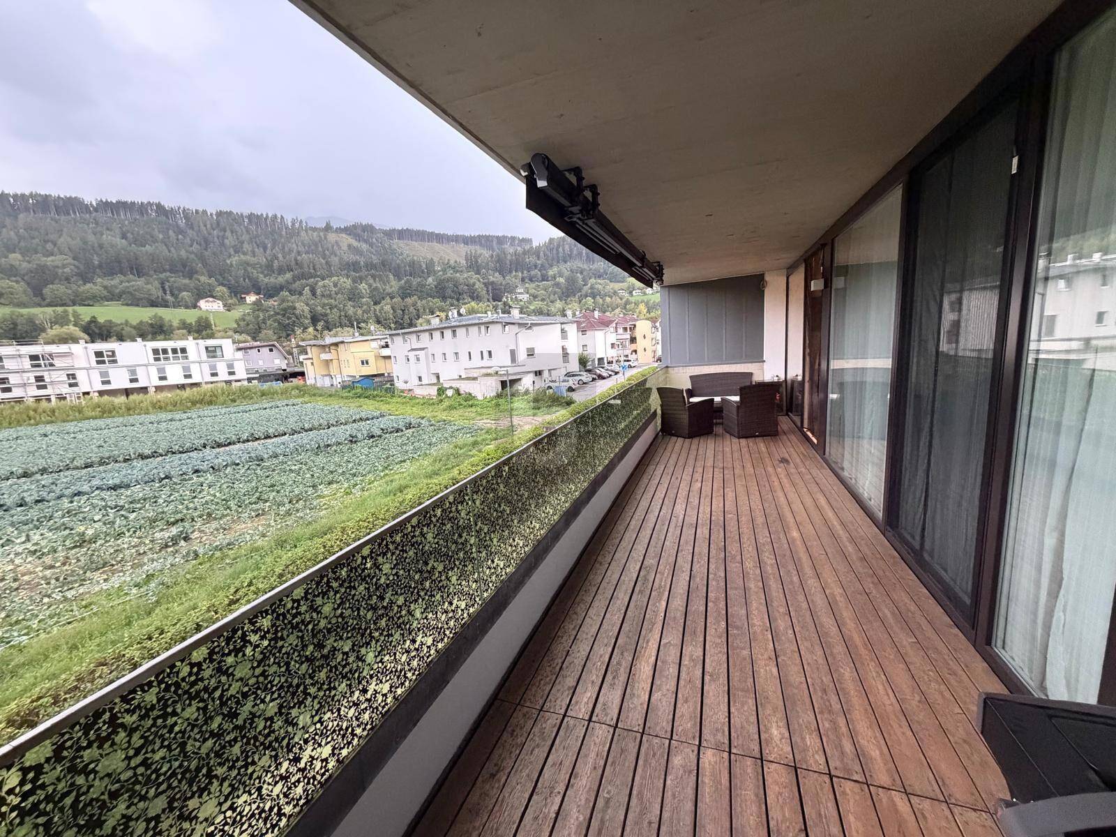 Langer Balkon mit Holzboden, Sitzgelegenheiten und Blick auf Felder und Hügel.